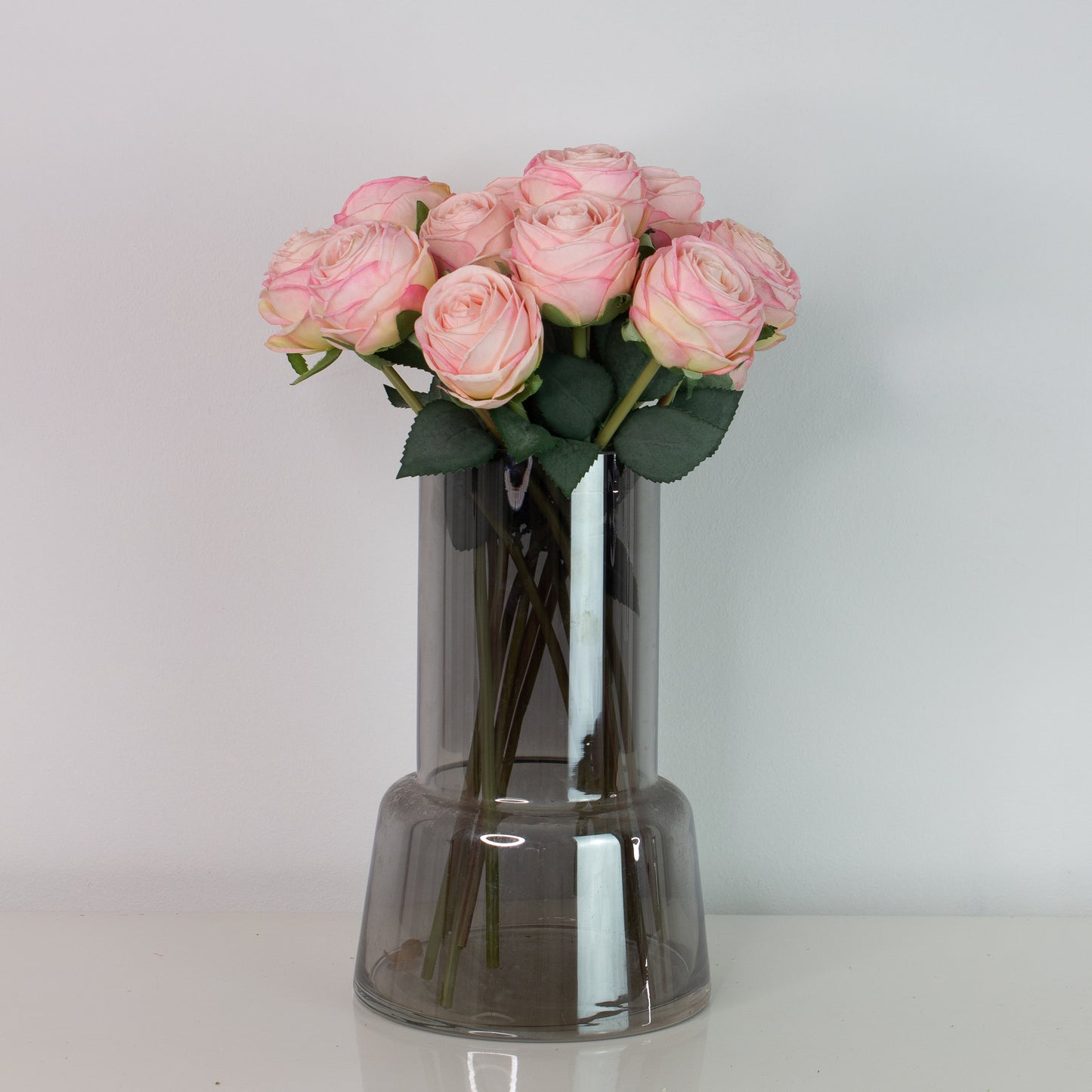 Pink naturtro roser i røgfarvet glasvase på hvid baggrund