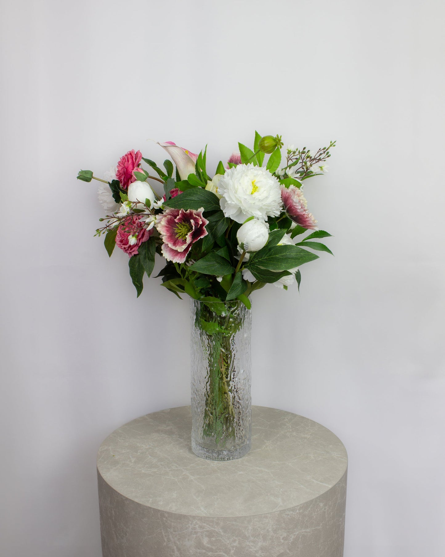 Naturtro kunstig buket i lyserøde og hvide nuancer i glasvase på piedestal.